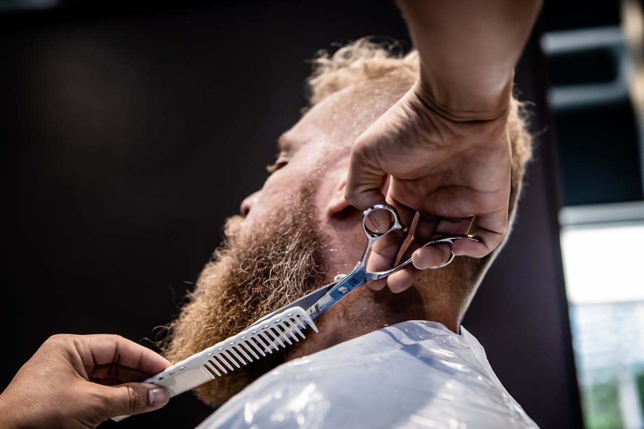 Barber shaping a beard with scissors and comb.